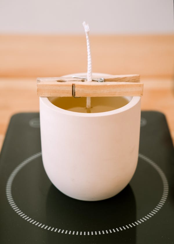 Close-up of a candle-making process with clothes pin holding wick in place.